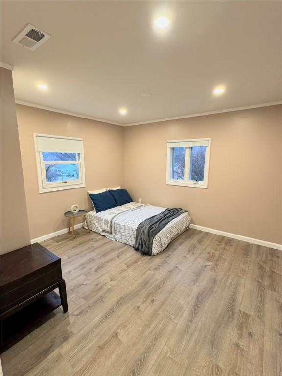 bedroom with visible vents, crown molding, baseboards, and wood finished floors