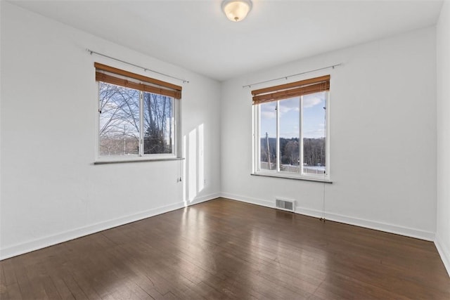 empty room with plenty of natural light, visible vents, and dark wood finished floors