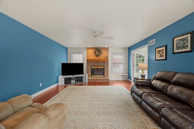 living area with a brick fireplace, visible vents, baseboards, and wood finished floors