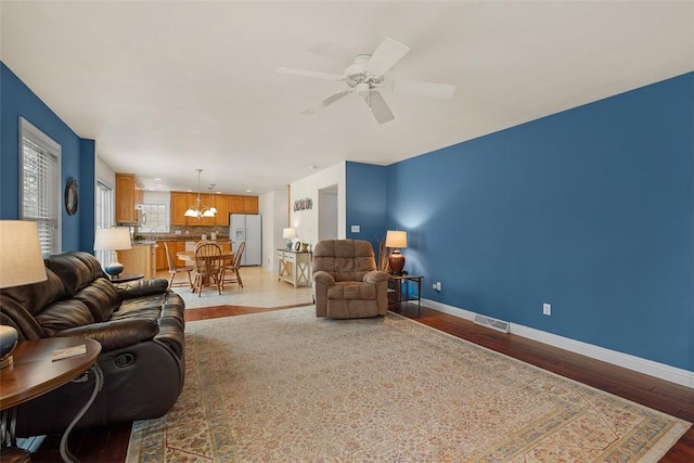 living area with baseboards, ceiling fan with notable chandelier, visible vents, and light wood-style floors