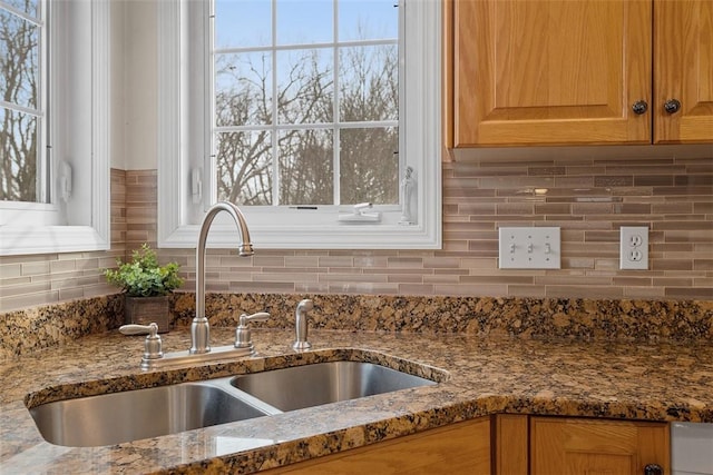 kitchen featuring a wealth of natural light, tasteful backsplash, a sink, and stone countertops