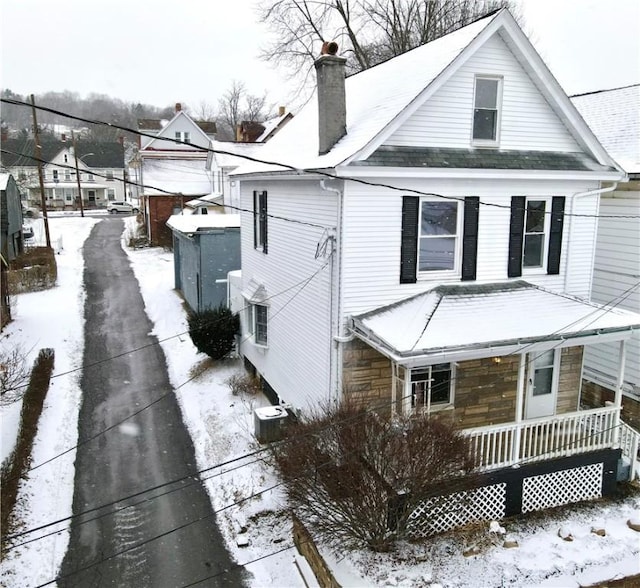 view of snowy exterior with central air condition unit, stone siding, a chimney, and covered porch