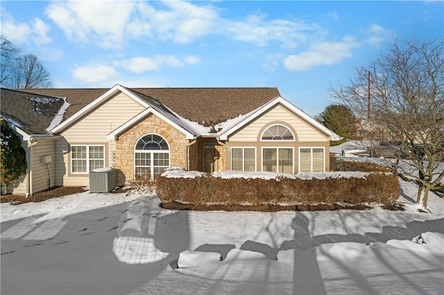 exterior space featuring a shingled roof, stone siding, and central air condition unit