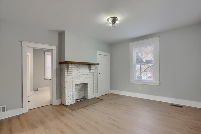 unfurnished living room featuring a brick fireplace, baseboards, visible vents, and light wood-style floors