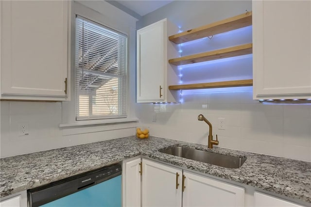 kitchen featuring light stone counters, backsplash, stainless steel dishwasher, white cabinetry, and a sink