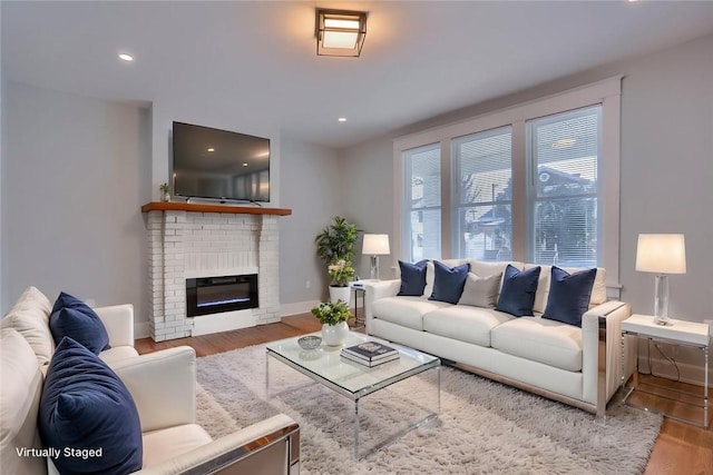living room with wood finished floors, a brick fireplace, recessed lighting, and baseboards