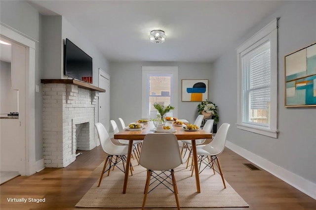 dining space with wood finished floors, a brick fireplace, and baseboards