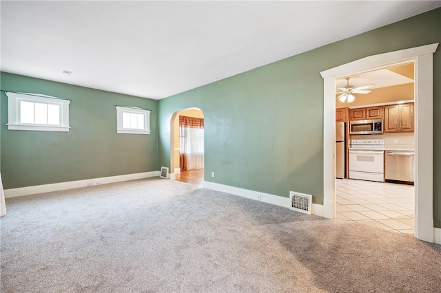 empty room featuring arched walkways, light colored carpet, visible vents, light tile patterned flooring, and baseboards