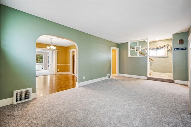 carpeted spare room with plenty of natural light, stairs, visible vents, and arched walkways