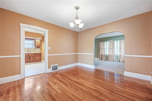 unfurnished room featuring light wood finished floors, baseboards, visible vents, arched walkways, and a chandelier