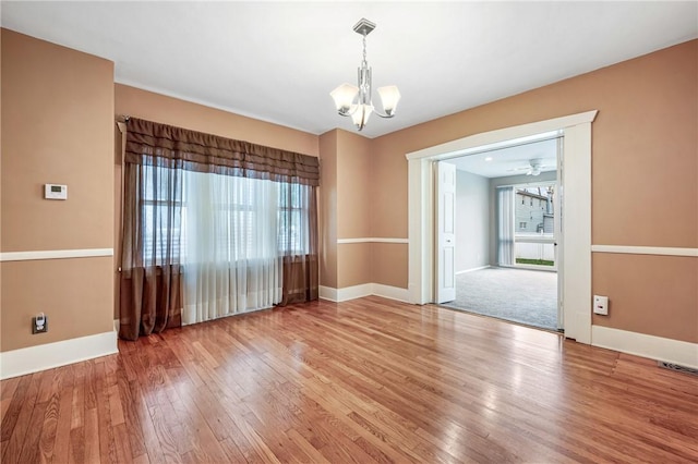 spare room with a chandelier, plenty of natural light, wood finished floors, and baseboards