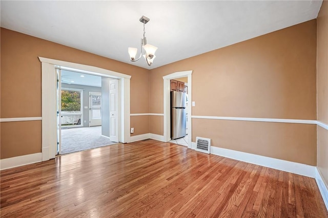 empty room with baseboards, visible vents, light wood finished floors, and an inviting chandelier