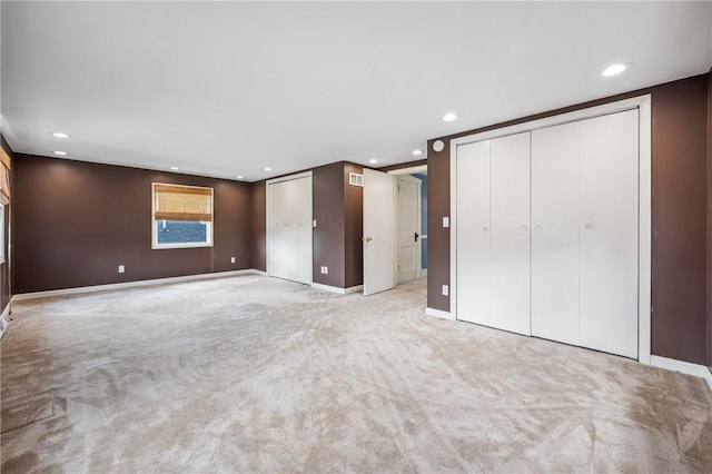 unfurnished bedroom with recessed lighting, two closets, and light colored carpet