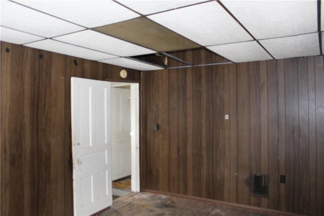 interior space with a drop ceiling and wood walls