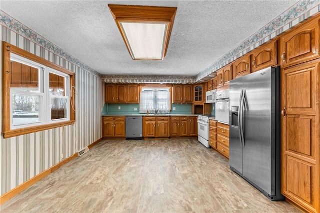 kitchen featuring wallpapered walls, brown cabinetry, glass insert cabinets, stainless steel appliances, and light countertops