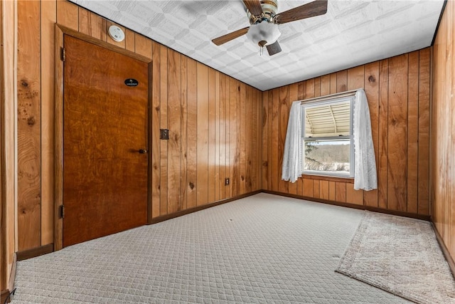 spare room with baseboards, light carpet, a ceiling fan, and wooden walls