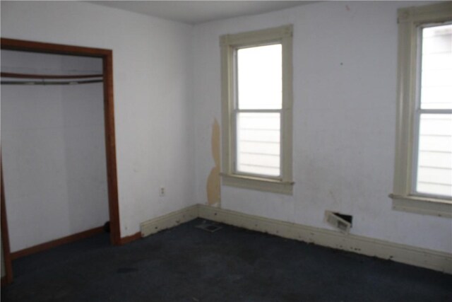 unfurnished bedroom with a closet, multiple windows, dark carpet, and baseboards