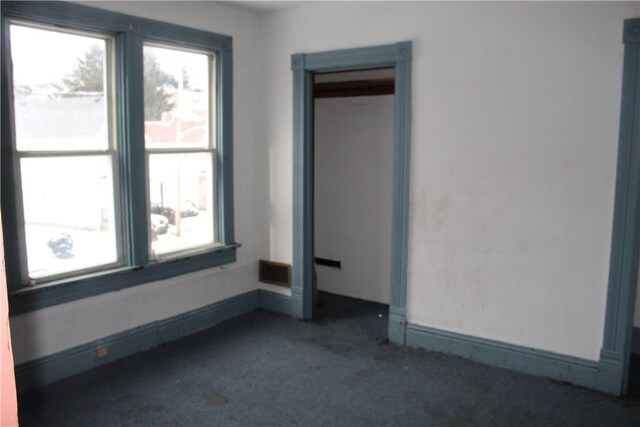 unfurnished room featuring baseboards and dark carpet