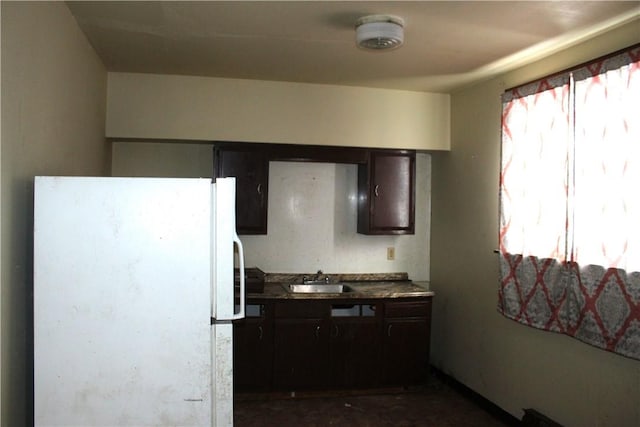 kitchen with dark brown cabinetry, a sink, and freestanding refrigerator