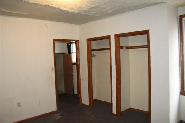 unfurnished bedroom with multiple closets, a textured ceiling, and baseboards