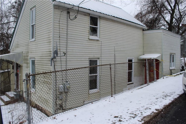 view of snowy exterior with fence and metal roof