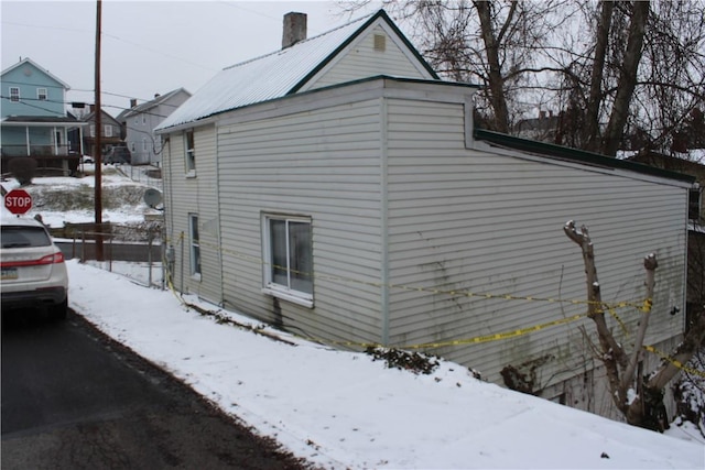 view of snowy exterior featuring metal roof and a chimney