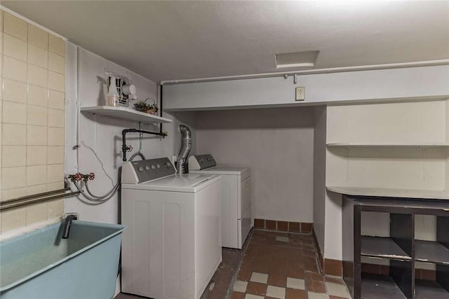 laundry area with laundry area, baseboards, dark floors, washing machine and clothes dryer, and a sink