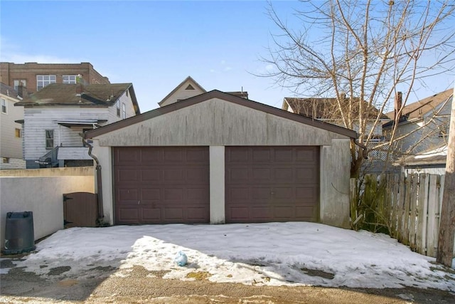 snow covered garage with a detached garage and fence