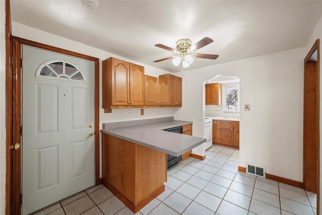 kitchen featuring a peninsula, brown cabinetry, black dishwasher, and light countertops