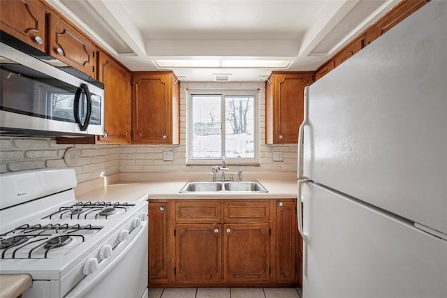 kitchen with brown cabinets, light tile patterned floors, light countertops, a sink, and white appliances