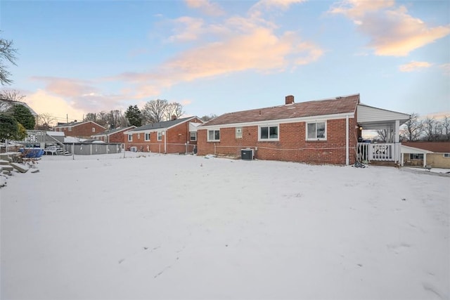 snow covered rear of property with brick siding, a chimney, and cooling unit