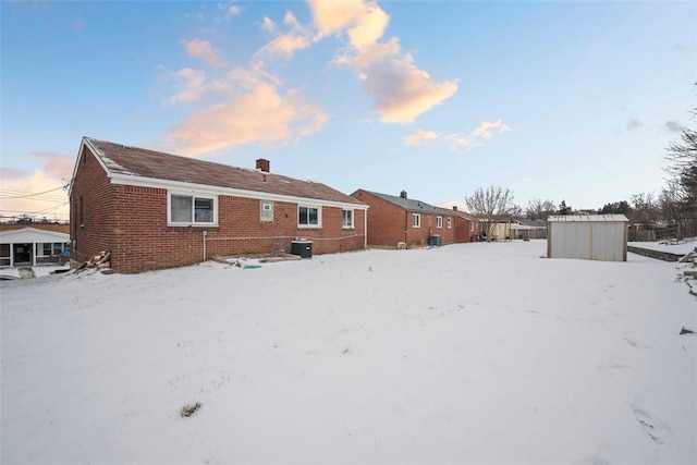 snow covered property featuring a shed, a chimney, an outbuilding, and brick siding