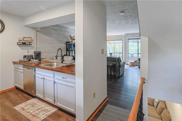 bar featuring stainless steel dishwasher, dark wood-style flooring, a sink, and baseboards