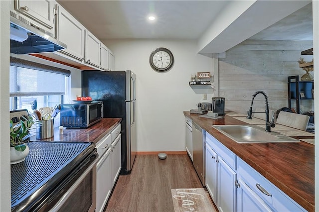 kitchen with stainless steel appliances, a sink, white cabinetry, wooden counters, and light wood-type flooring