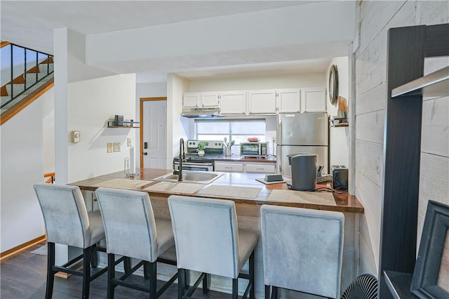 kitchen featuring dark wood finished floors, a kitchen breakfast bar, a peninsula, stainless steel appliances, and white cabinetry