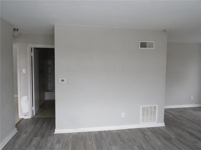 empty room featuring dark wood-type flooring, visible vents, and baseboards