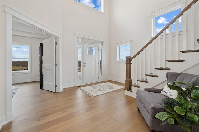 foyer featuring stairs, a high ceiling, light wood-style flooring, and baseboards