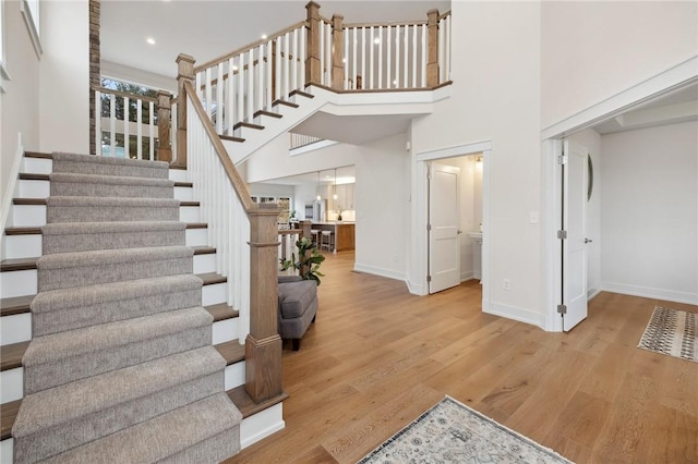 stairs featuring baseboards, a towering ceiling, wood finished floors, and recessed lighting