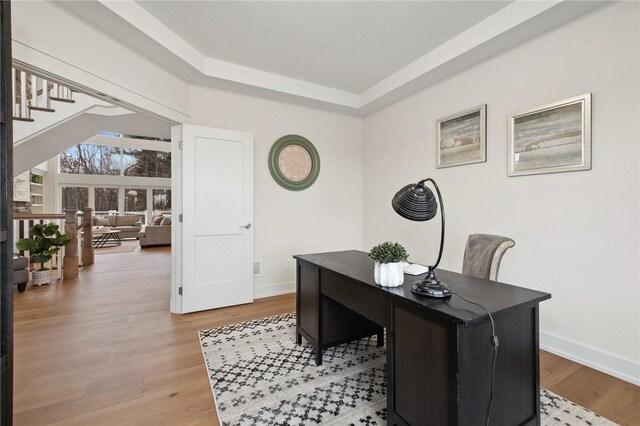 office with a tray ceiling, baseboards, and wood finished floors