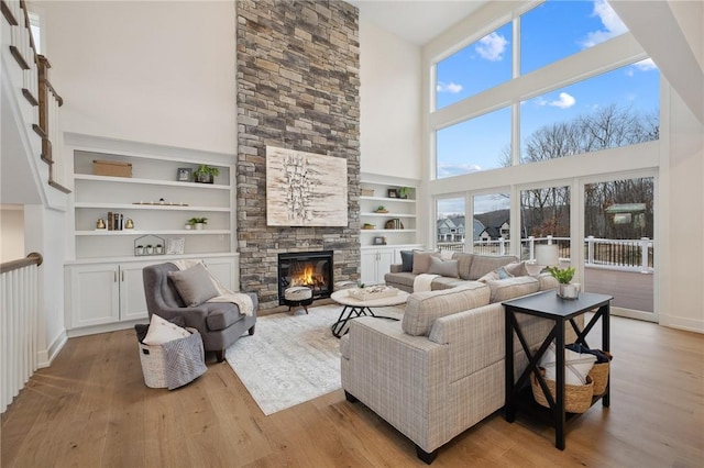 living area with built in shelves, wood finished floors, a towering ceiling, and a stone fireplace