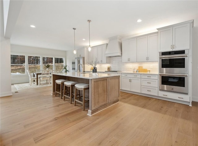 kitchen featuring custom range hood, cooktop, double oven, and light wood finished floors