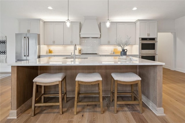 kitchen featuring custom range hood, a spacious island, a sink, light wood-style floors, and appliances with stainless steel finishes