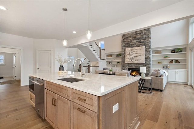 kitchen featuring light wood finished floors, a fireplace, light stone countertops, a sink, and stainless steel dishwasher