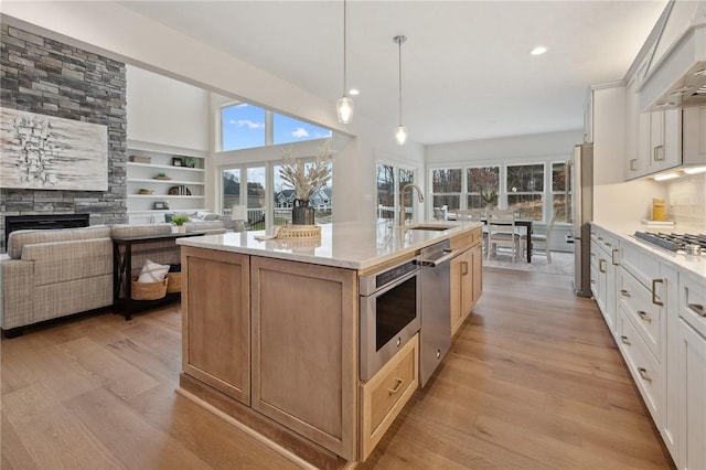 kitchen featuring a sink, a center island with sink, custom exhaust hood, stainless steel appliances, and light wood-style floors