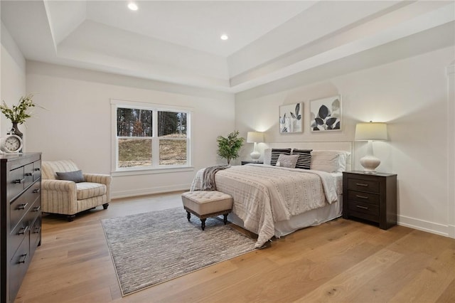 bedroom featuring light wood-style flooring, a tray ceiling, baseboards, and recessed lighting