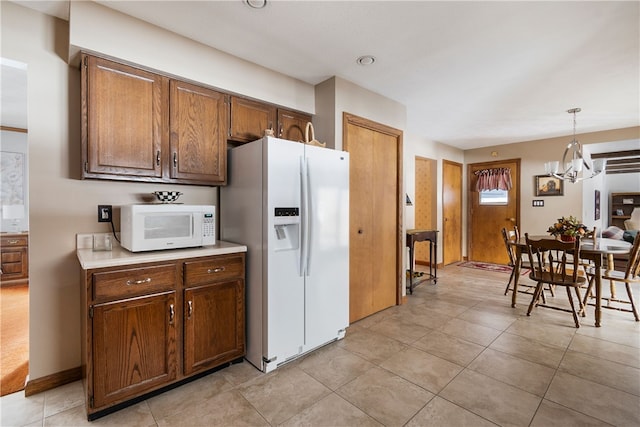 kitchen featuring light tile patterned flooring, white appliances, brown cabinetry, light countertops, and hanging light fixtures