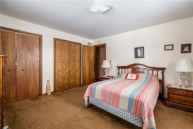 bedroom featuring multiple closets, visible vents, a textured ceiling, and carpet flooring