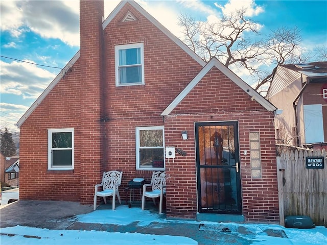 view of front facade with brick siding, a chimney, and fence