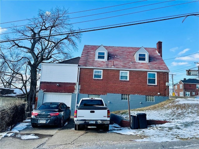 view of snow covered exterior with driveway, a chimney, and brick siding