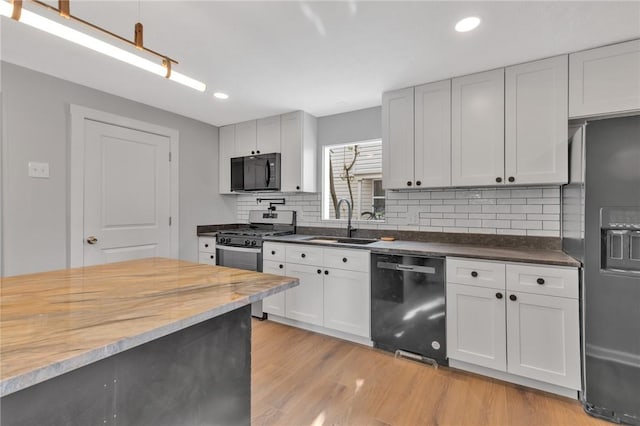 kitchen featuring a sink, light wood-style floors, white cabinets, backsplash, and black appliances